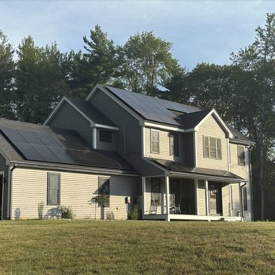Colonial on an open lot with black solar panels on the main roof