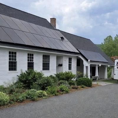 White farmhouse with a large black solar array and the Old Glory van